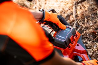 Una persona che regola le impostazioni di un robot tagliaerba Husqvarna in un giardino.