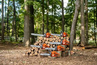 Six Husqvarna chainsaws displayed on a stack of cut tree logs in a forest setting.