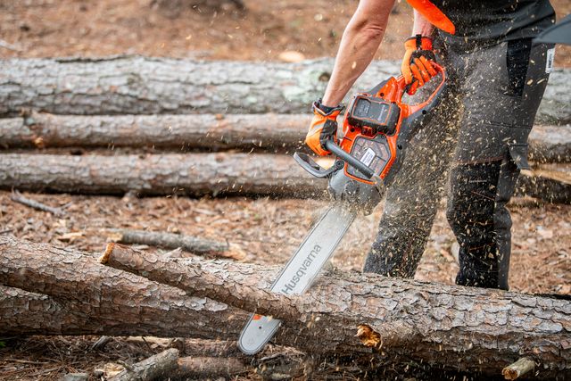 Henkilö, joka käyttää Husqvarna-moottorisahaa puun leikkaamiseen metsässä.