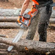 A person using a Husqvarna chainsaw to cut tree logs in a forest setting.