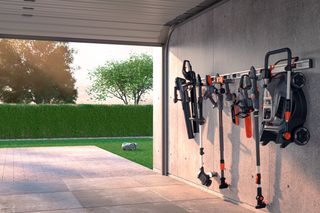 Attrezzi da giardinaggio ordinatamente organizzati su un appendiabiti a muro in un garage, con vista su un giardino esterno.