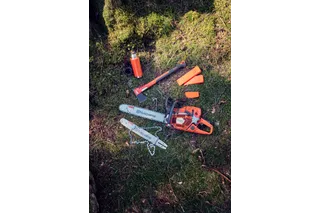 Motorová píla, sekera a ochranné pomôcky Husqvarna položené na lesnej pôde.