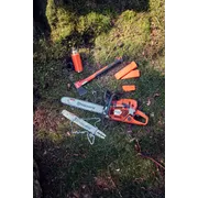 Motorová píla, sekera a ochranné pomôcky Husqvarna položené na lesnej pôde.