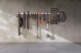 A set of gardening tools hanging on a wall rack in a garage setting.
