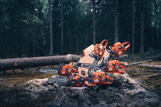 En samling motorsågar från Husqvarna visas på marken i skogen med nedfallna träd i bakgrunden.
