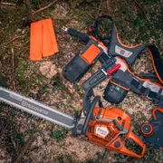 Motorová píla a pracovné vybavenie Husqvarna položené na lesnej pôde.
