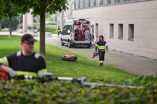 Un travailleur transporte de l’équipement en direction d’une camionnette garée à l’extérieur d’un bâtiment moderne.