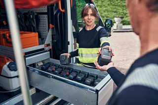 Two people exchanging batteries from a storage drawer in a utility vehicle.