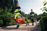Двоє робітників у саду, один з яких тримає ящик з інструментами Husqvarna та ланцюгову пилку, інший тримає тример і повітродув для листя.