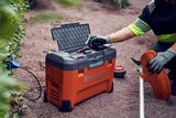 Людина, яка готує акумуляторний інструмент Husqvarna із зарядним пристроєм і приладдям на гравійній доріжці.