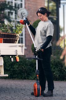 A person holding a gardening tool next to a vehicle equipped with various gardening products.