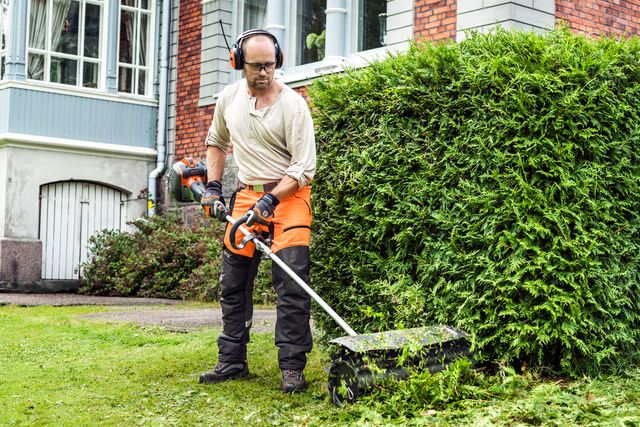 A person using a hedge trimmer to trim a bush in a garden setting.