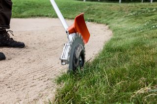 A person using a grass trimmer to edge a lawn next to a sand bunker.