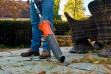 A person using a leaf blower to clear fallen leaves on a patio.