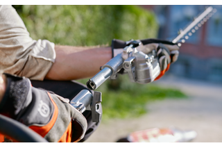 A person using a hedge trimmer attachment on a pole in a garden setting.
