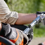 A person using a hedge trimmer attachment on a pole in a garden setting.
