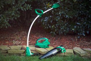 A set of garden tools including a string trimmer and a leaf blower placed on a stone border in a garden.