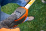 Close-up of a person wearing work gloves holding a gardening tool handle with a control button.