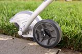 Close-up of a Husqvarna lawn edger wheel and blade on grass and pavement.