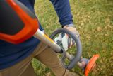 A person using a grass trimmer on a lawn, focusing on the handle and control grip.