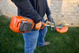 A person holding a battery-powered grass trimmer, showcasing the battery compartment.