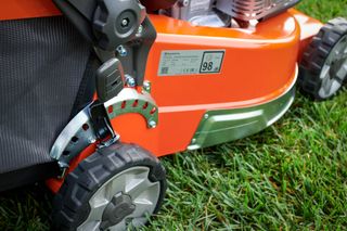 Close-up of a lawn mower wheel and adjustment lever on grass.