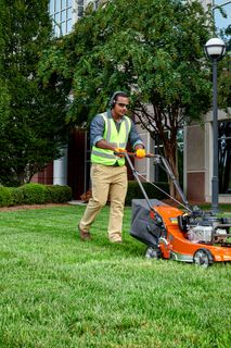 A person mowing a lawn with a push mower in a landscaped garden area.