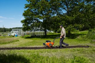 A person using a tiller to cultivate soil in a garden setting.