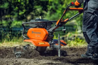 Uma pessoa a utilizar uma motoenxada Husqvarna em solo de jardim.