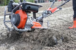 A Husqvarna construction tool in action, mixing soil on a construction site.