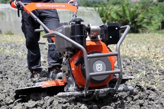 Una persona utiliza una motoazada Husqvarna para cultivar la tierra de un campo.