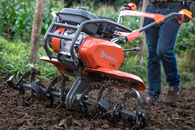 Una persona que utiliza una motoazada Husqvarna para cultivar la tierra de un jardín.