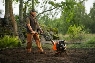 Husqvarna TF 120. Person, die eine handgeführte Husqvarna Motorhacke auf dem Boden eines Gartens bedient.