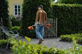 En person som går på en grusgång i en trädgård omgiven av frodig grönska.