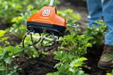 En person som använder ett trädgårdsredskap från Husqvarna för att bruka jord bland jordgubbsplantor.