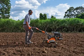 Uma pessoa usando uma motoenxada para cultivar o solo em um campo.