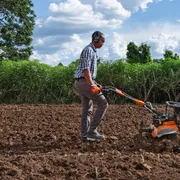 Uma pessoa usando uma motoenxada para cultivar o solo em um campo.
