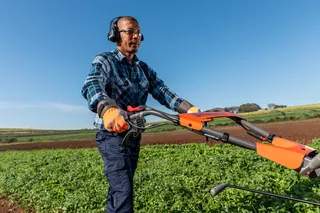 Uma pessoa que utiliza um cortador de relva num campo, utilizando equipamento de trabalho e auscultadores.