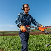 Uma pessoa que utiliza um cortador de relva num campo, utilizando equipamento de trabalho e auscultadores.