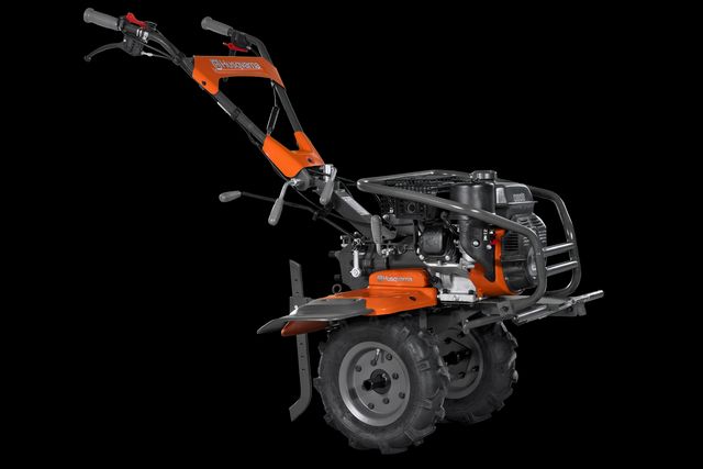 Вид збоку на культиватор Husqvarna, на якому видно елементи керування та двигун.