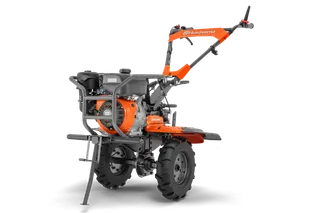 Husqvarna TF 545P. Side view of a Husqvarna walk-behind garden tiller showing handlebar, engine and treaded wheels.