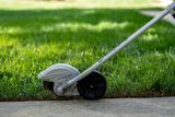 Close-up of a lawn edger being used on the edge of a grass lawn.