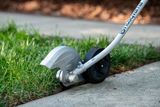 A Husqvarna edger trimming grass along a concrete pathway.