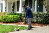 A person using a lawn edger to trim the grass along a sidewalk in a residential area.