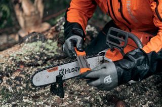 En person som slipar en motorsågskedja från Husqvarna på en nedfallen trädstam.