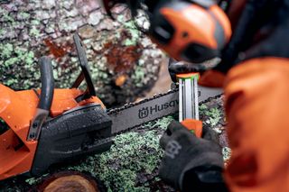 A person sharpening a Husqvarna chainsaw on a moss-covered log.