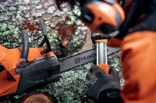 Uma pessoa a afiar uma motosserra Husqvarna num tronco coberto de musgo.