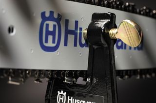 Close-up of a Husqvarna chainsaw chain tensioner with branding visible.