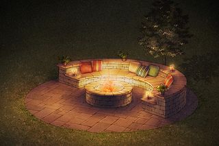 Outdoor circular stone seating area with a central fire pit, surrounded by cushions and candles.