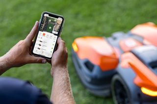 Une personne utilise une application pour smartphone pour contrôler un robot tondeuse dans un jardin.